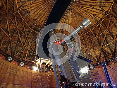 A telescope at Lowell Observatory with a view of Orion's belt and other stars visible in the sky out the window Stock Photo